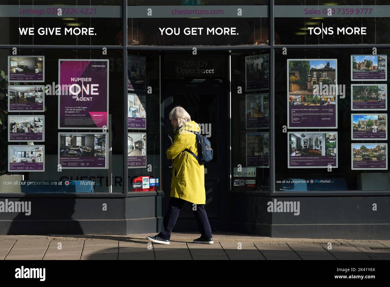 Un generale di una persona che cammina oltre gli annunci pubblicitari in una finestra di agenti immobiliari a Islington, nel nord di Londra. Foto Stock