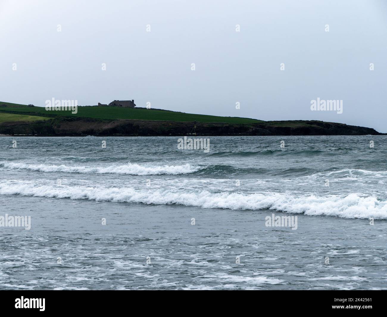 Mare con alta marea. Un edificio su una collina. Cielo grigio, edificio su prato verde vicino al mare. Paesaggio marino, schiuma bianca sulle onde. Foto Stock