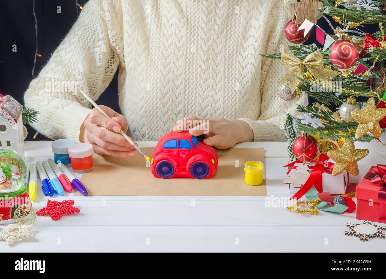 Istruzioni fotografiche passo-passo di una decorazione natalizia - una ragazza dipinge un'auto in gesso, passo 6 - colorando i fari con vernice gialla Foto Stock