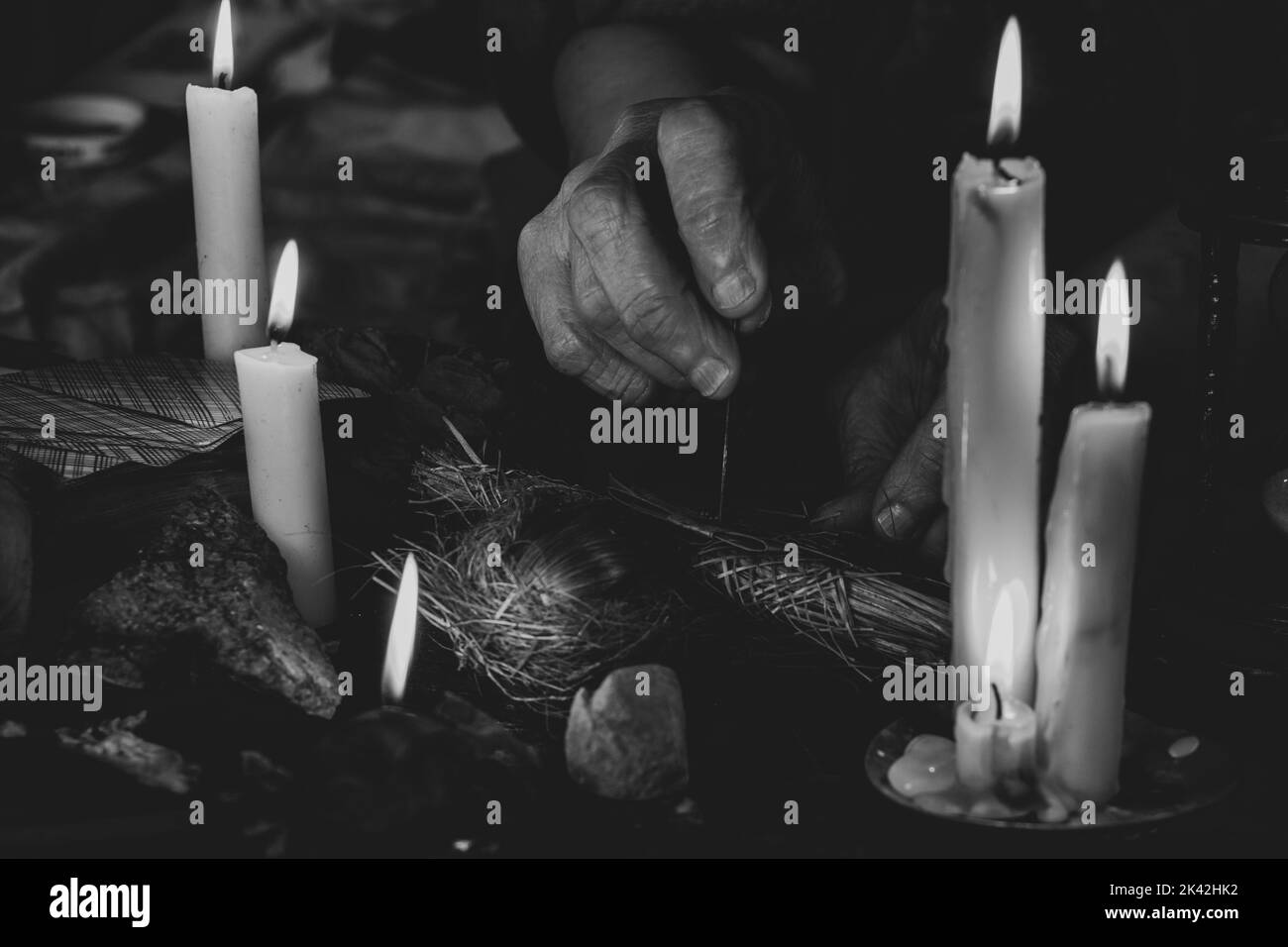Voodoo bambola nelle mani di una vecchia strega con un ago nel cuore al buio sullo sfondo di candele, maledizioni e magia nera Foto Stock
