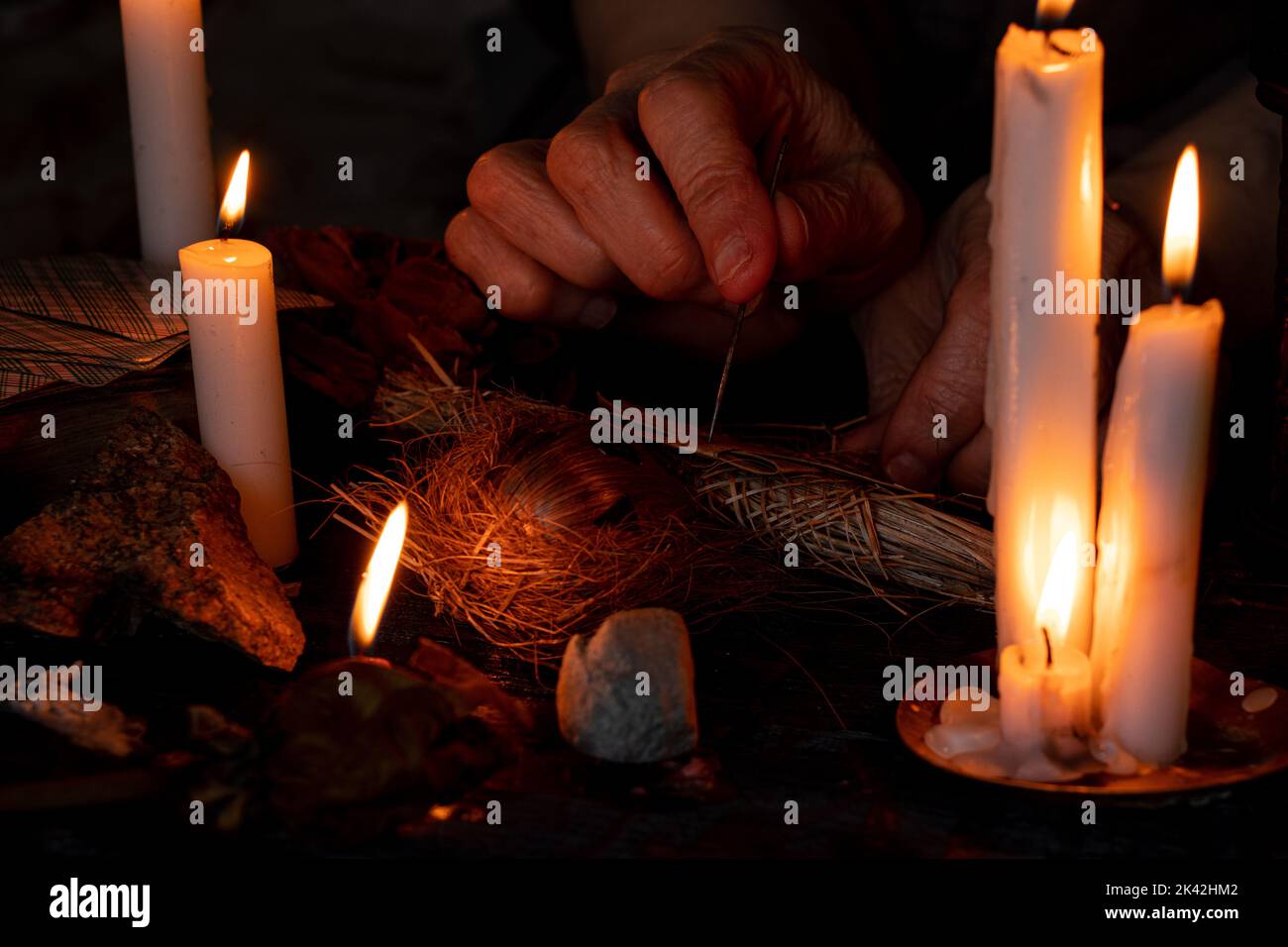 Voodoo bambola nelle mani di una vecchia strega con un ago nel cuore al buio sullo sfondo di candele, maledizioni e magia nera Foto Stock