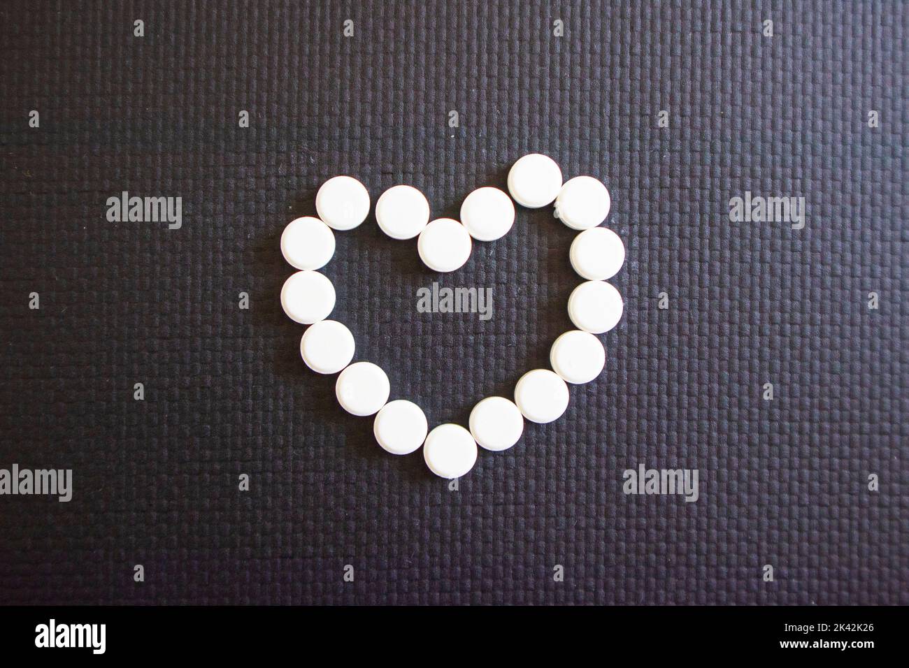 pillole bianche a forma di cuore su uno sfondo nero. malattie cardiache Foto Stock