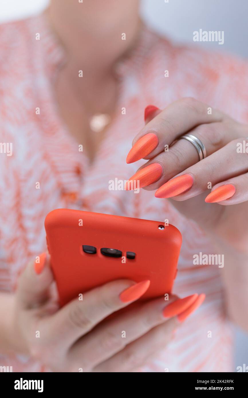 Le mani di una donna che tiene in mano un grande smartphone di corallo Foto Stock