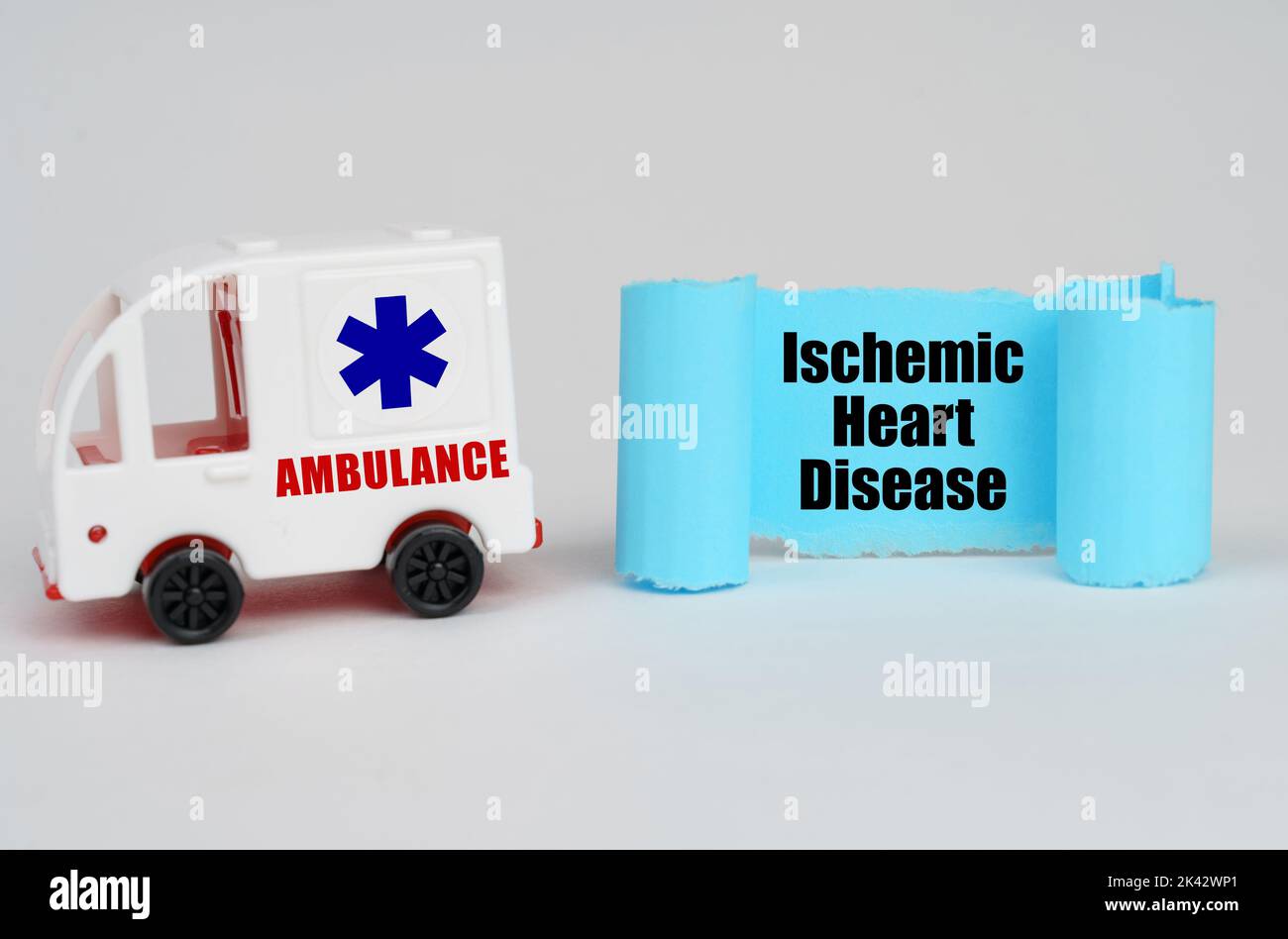 Concetto medico. Su una superficie bianca, un'ambulanza e un segno di carta blu con l'iscrizione - cardiopatia ischemica Foto Stock