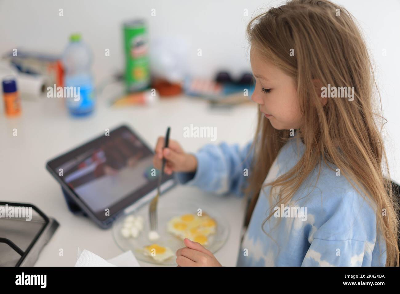 Positiva bambina caucasica che fa colazione e guarda il tablet a casa Foto Stock