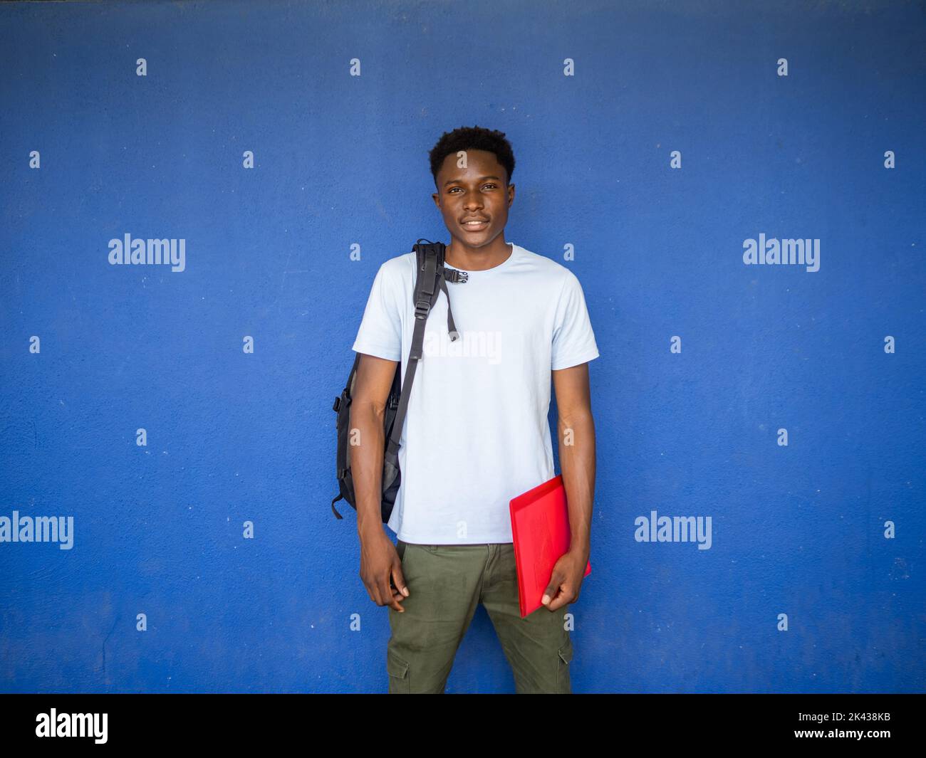 Ritratto di un giovane studente afro-americano che guarda la fotocamera con uno zaino e una cartella. Ritorno a scuola, scuola superiore, università Foto Stock