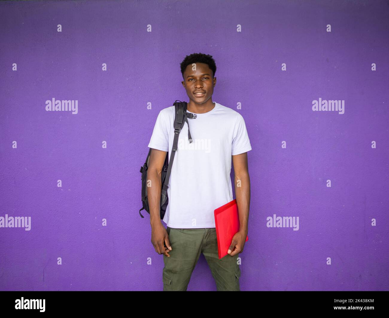 Ritratto di un giovane studente afro-americano che guarda la fotocamera con uno zaino e una cartella. Ritorno a scuola, scuola superiore, università Foto Stock