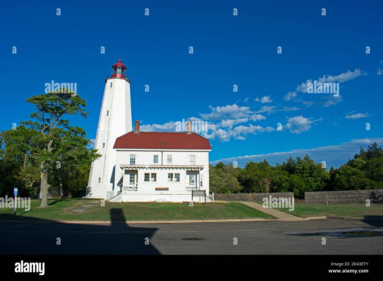 Faro a Sandy Hook, New Jersey, con ombre nel tardo pomeriggio e un cielo blu parzialmente nuvoloso -77 Foto Stock