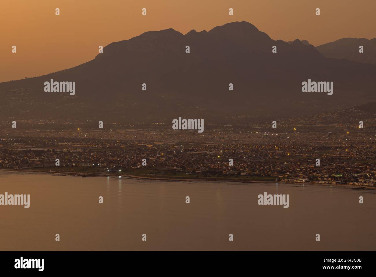 Paesaggio di mare, riva del mare con le luci della città, montagne, cielo senza nuvole al tramonto e all'orizzonte Foto Stock