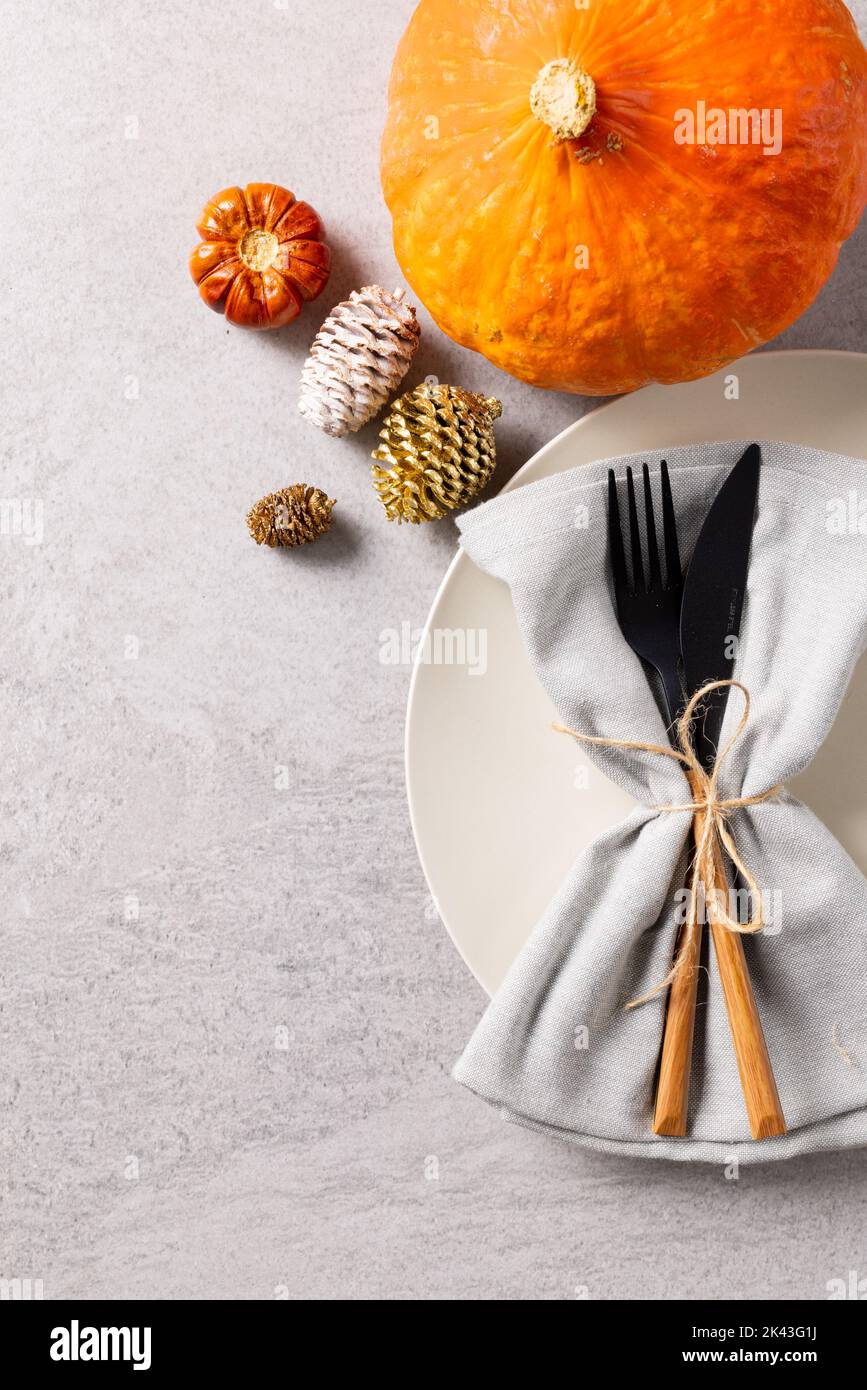 Vista dall'alto del piatto con posate e tovagliolo, zucca, coni di pino e spazio copia su grigio Foto Stock