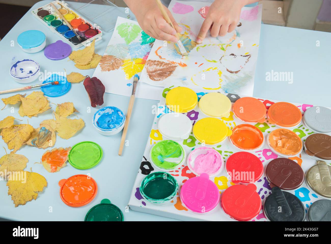 Bambino sta dipingendo e disegnando con acquerelli e colori delle dita. Stampa delle foglie sulla carta. Bambini che giocano, educano in belle arti. Bambini creatività. Foto Stock