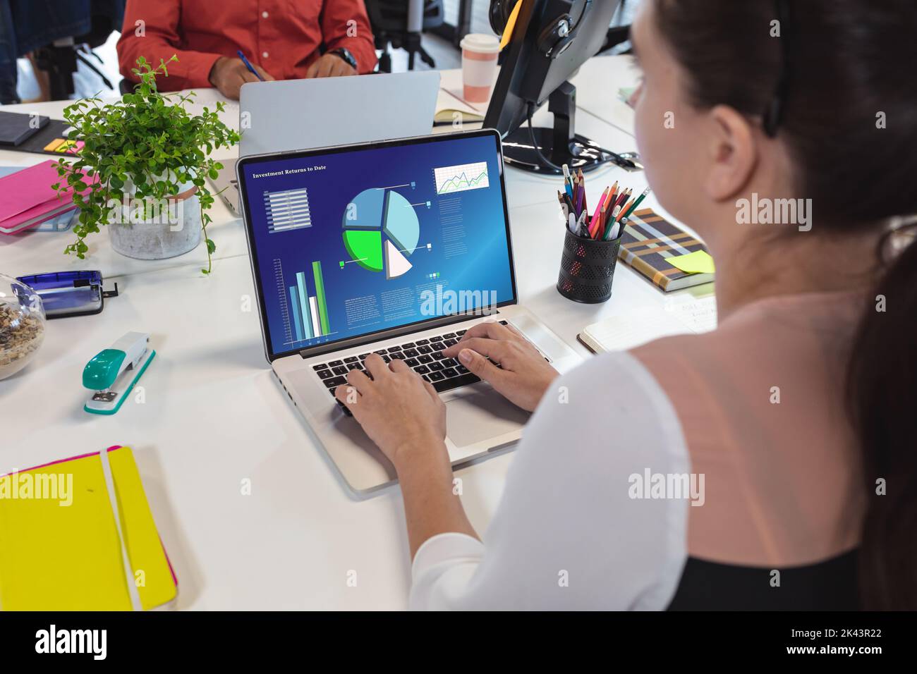 Giovane donna d'affari caucasica che analizza le tabelle di affari sopra il laptop in ufficio Foto Stock