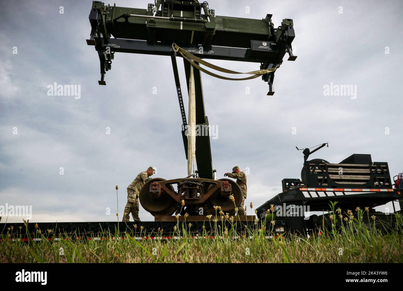 I soldati della guardia nazionale dell'esercito dell'Iowa con il Dipartimento dei lavori pubblici e il Centro di addestramento per la sostenibilità del campo (Camp Dodge) assicurano un set di camion ferroviari storici per il trasporto a Camp Dodge a Johnston, Iowa, il 3 agosto 2022. Tre vagoni ferroviari a pianale, una rampa e un breve tratto di binario furono installati a Camp Dodge negli anni '1980s e servirono come sito di addestramento per i soldati per diversi anni prima che le operazioni ferroviarie diventassero in gran parte obsolete nella Guardia Nazionale dell'Iowa. Le vagoni si sono arenate su carrelli con cuscinetti di attrito originali, che non sono più utilizzati nelle moderne ferrovie con cuscinetti a rulli. Piuttosto che rottamare Foto Stock