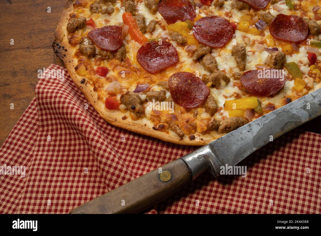 Pizza su tavola di legno con coltello antico e panno rosso assegno Foto Stock