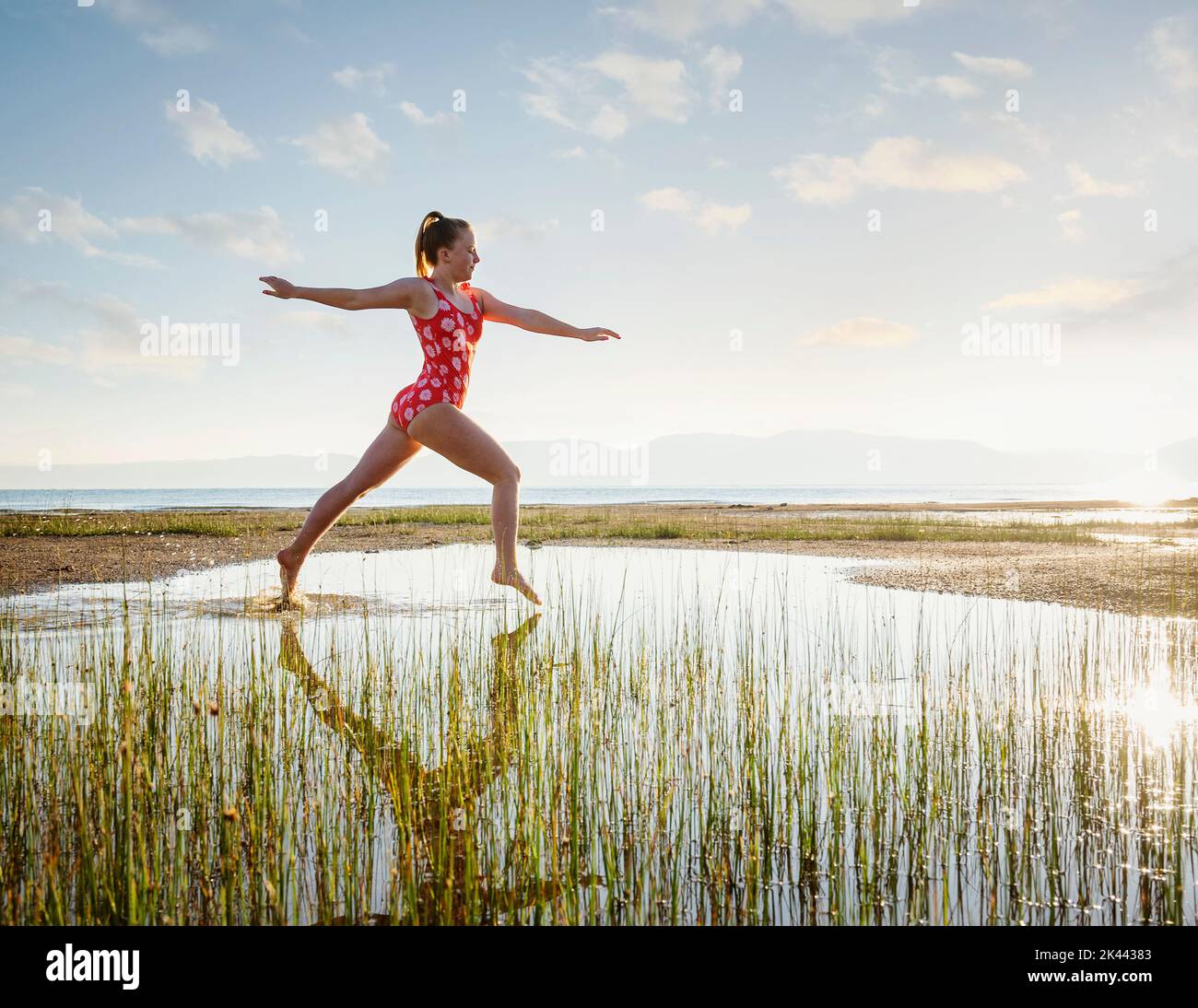 Ragazza (12-13) in costume da bagno che salta sopra il lago all'alba Foto Stock