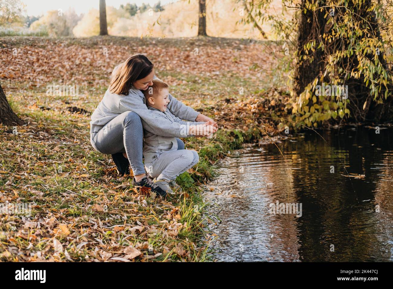 Madre con bambini pesca con un bastone al bordo di un lago nel parco autunnale. Natura selvaggia e divertimento in acqua durante le vacanze autunnali. Campeggio e pesca Foto Stock