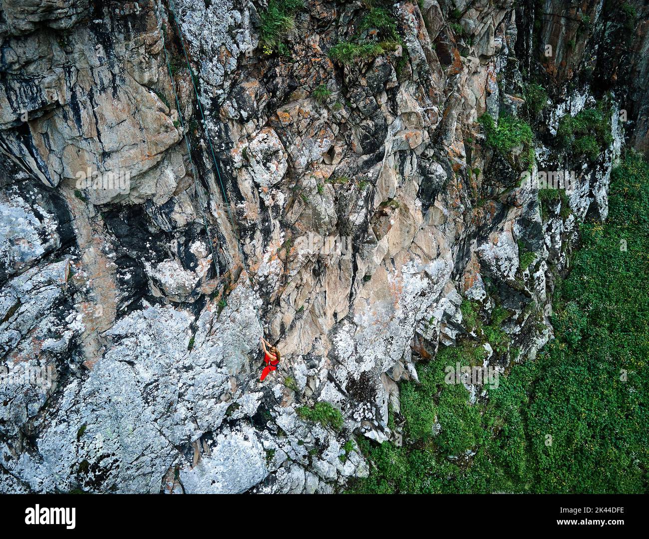 Drone colpo di donna forte in camicia rossa arrampicata sulla roccia alta sulle montagne Tyan Shan in Kazakhstan Foto Stock