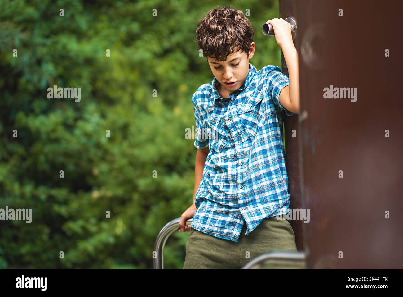 Un bambino si arrampica nel parco giochi per bambini del parco - un bambino esegue attività motorie all'aperto arrampicandosi sui picchetti al parco giochi all'aperto - p Foto Stock