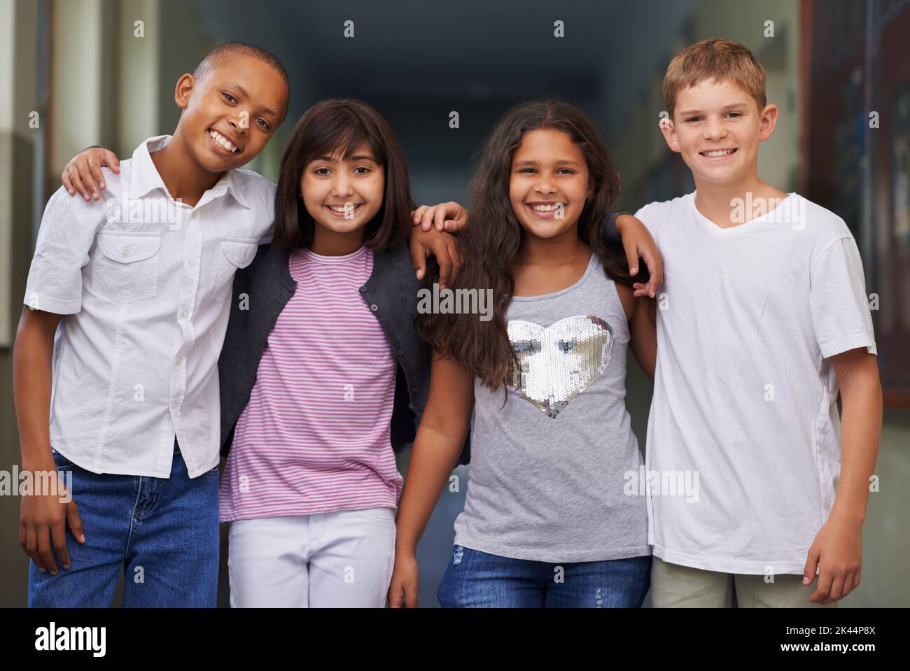 Amici della scuola. Quattro amici in piedi braccio-in-braccio nel corridoio della loro scuola. Foto Stock