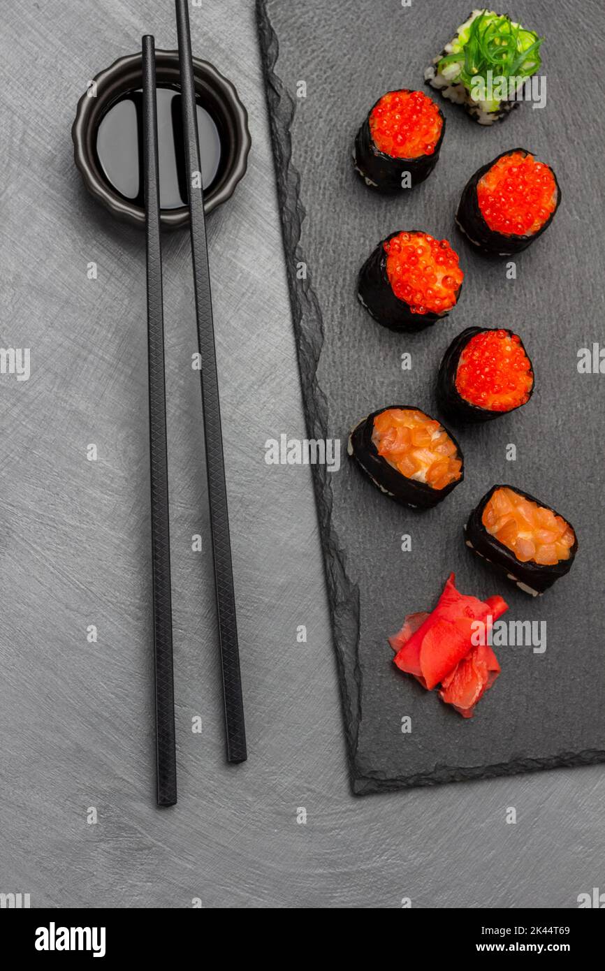Sushi con caviale e salmone su tavola di pietra. Chopsticks su ciotola con salsa. Giacitura piatta. Sfondo grigio. Foto Stock