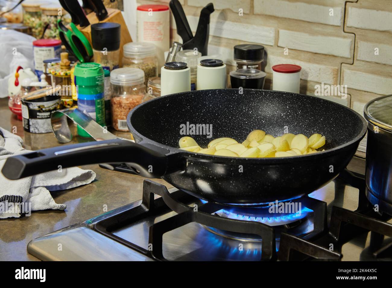 Le patate a fette vengono fritte in padella su stufa a gas Foto Stock