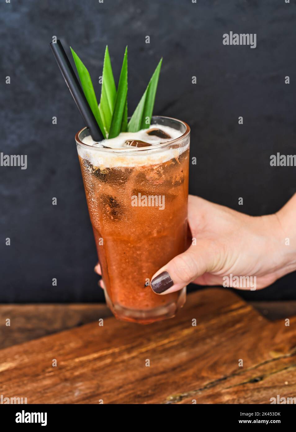 Mano che tiene il tè tropicale ghiacciato fatto di tè verde e marmellata d'arancia su sfondo tavolo di legno Foto Stock