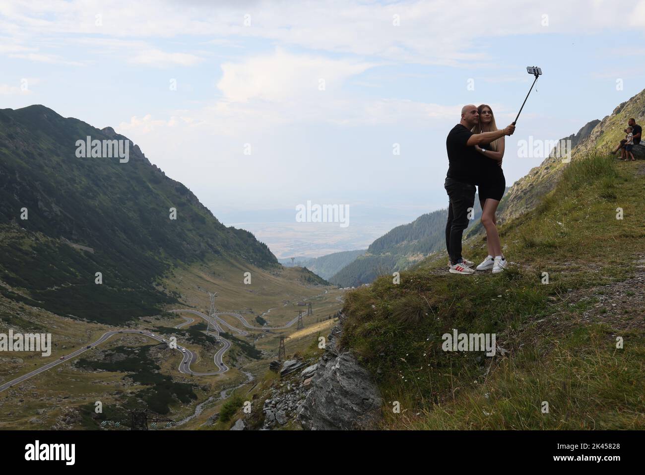 Coppia, tenendosi l'un l'altro, facendo un selfie con un selfie-bastone lungo la strada Transfagarasan, con una bella vista sullo sfondo Foto Stock