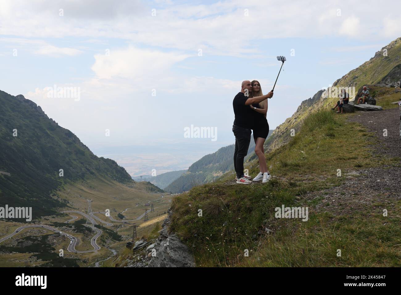 Coppia, tenendosi l'un l'altro, facendo un selfie con un selfie-bastone lungo la strada Transfagarasan, con una bella vista sullo sfondo Foto Stock