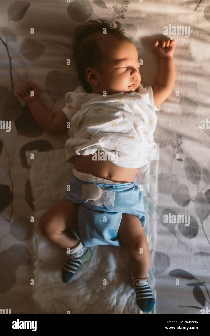 neonato con pannolino in tessuto che dorme tranquillamente a letto al mattino con luce naturale e pijama bianca Foto Stock