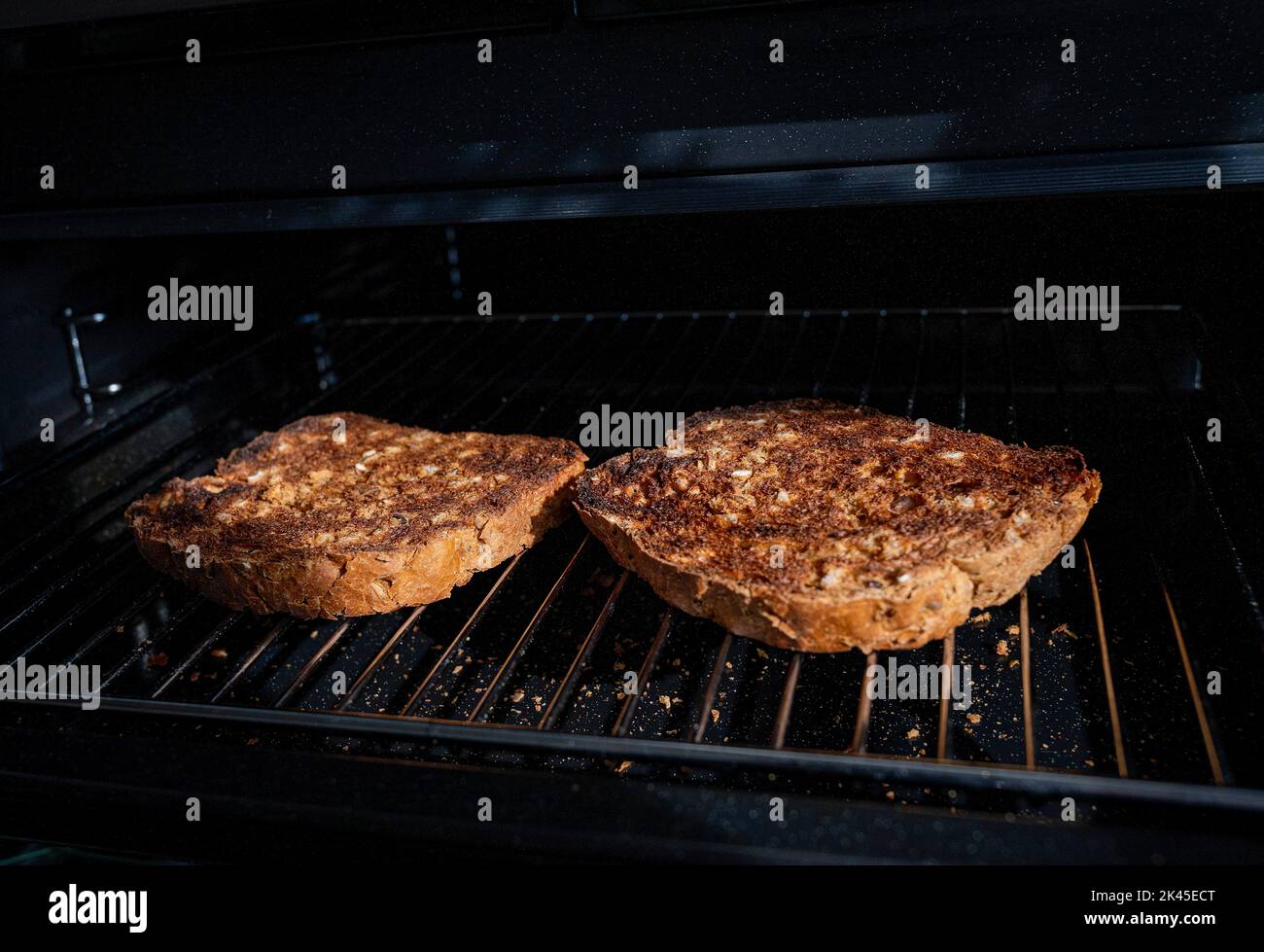 Preparare il pane tostato con pane al granaio marrone sotto una griglia elettrica in cucina Foto Stock