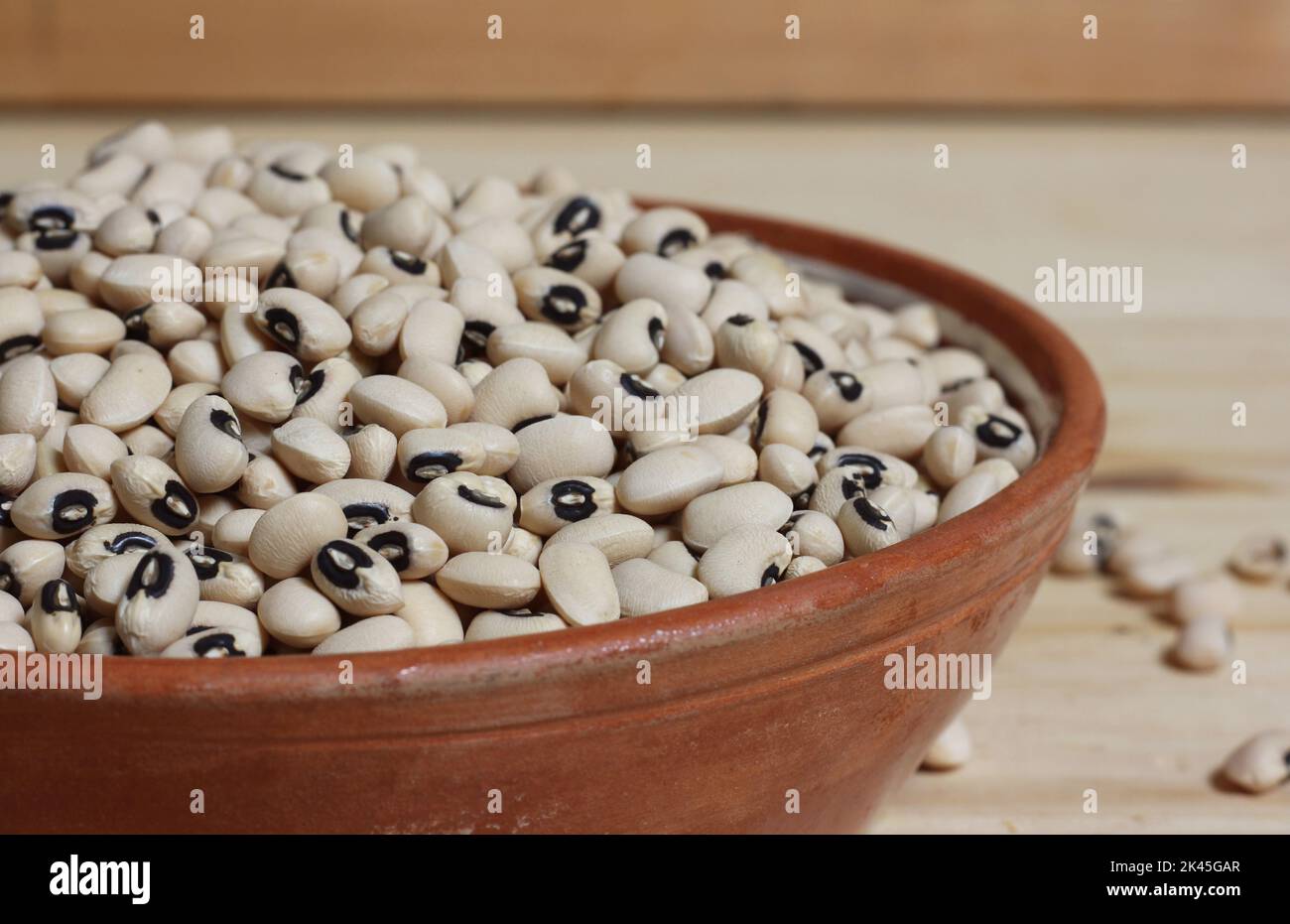 Piselli secchi neri secchi non cotti in ciotola su tavola di legno Foto Stock