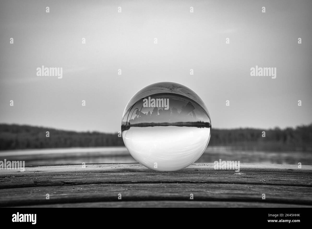 Palla di vetro su un molo di legno presso un lago svedese al crepuscolo in bianco e nero. Foto della natura dalla Scandinavia Foto Stock