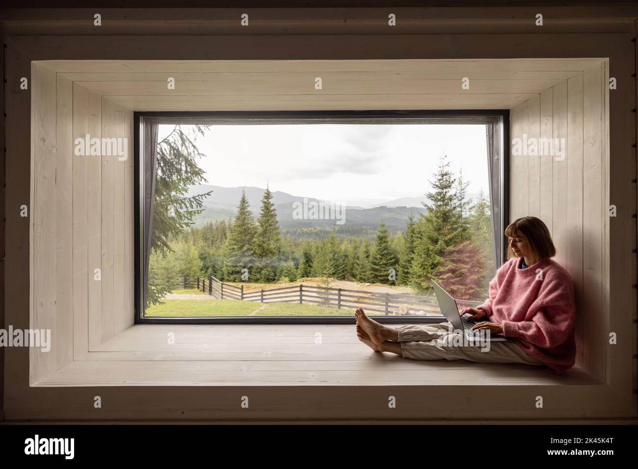 Donna lavora su un computer portatile a casa in montagna Foto Stock