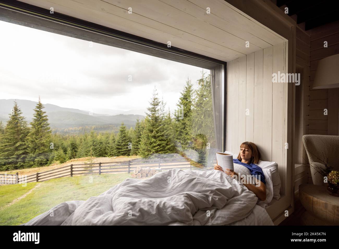 Donna con un libro sdraiato su una finestra davanzale in casa sulle montagne Foto Stock