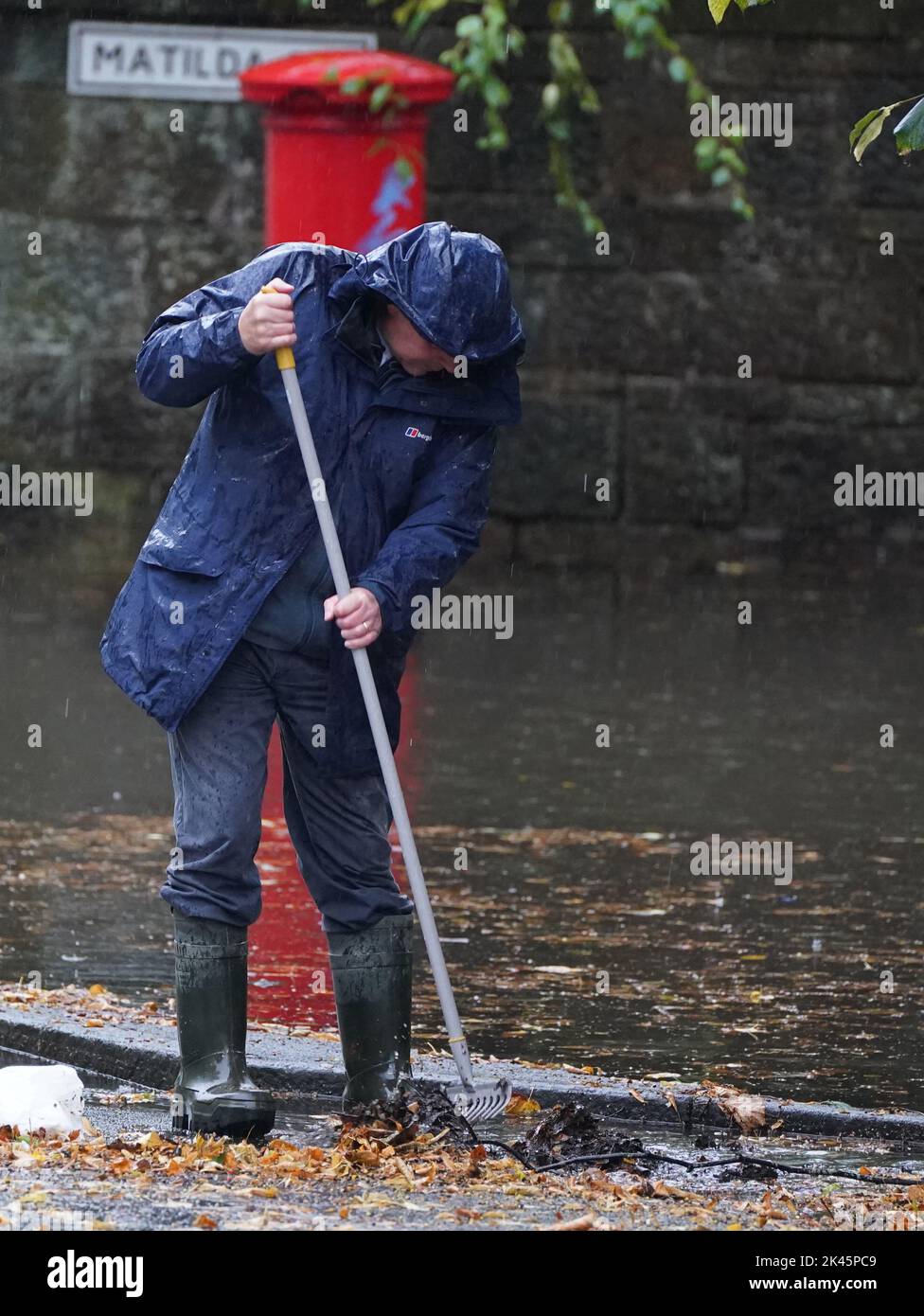 Un uomo cerca di facilitare le alluvioni eliminando i detriti autunnali dagli scarichi durante le forti precipitazioni a Glasgow. Data immagine: Venerdì 30 settembre 2022. Foto Stock