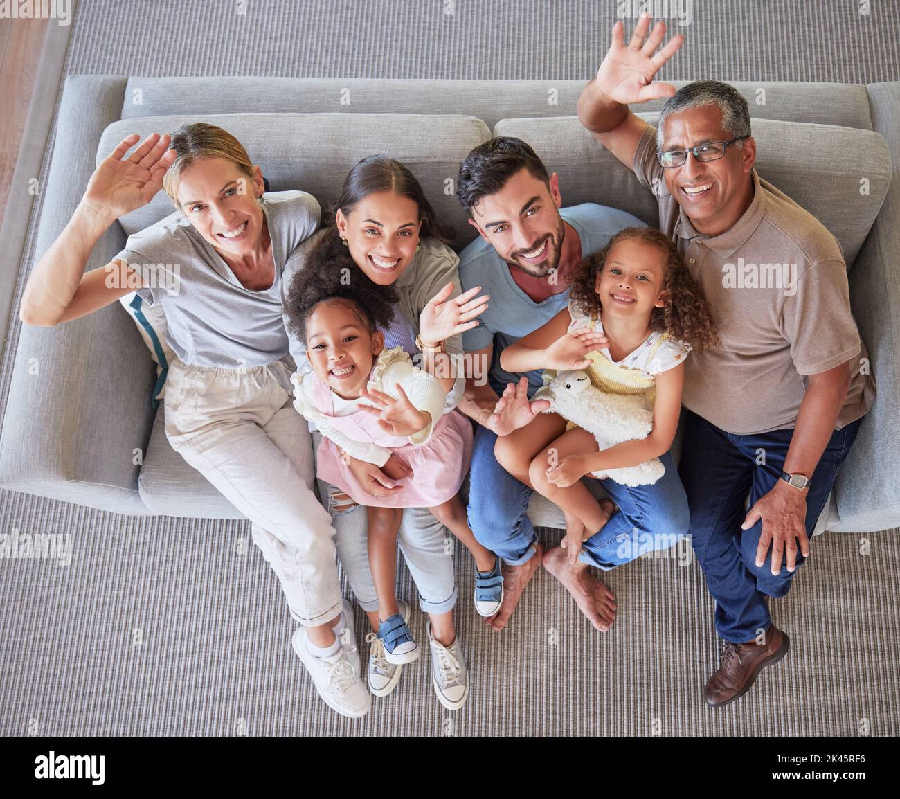 Le mani, le onde e l'ampia vista dall'alto per tutta la famiglia sul divano o sul divano nel soggiorno di casa. Ritratto di mamma, papà e ragazze che si prendono cura di loro con nonni in casa Foto Stock