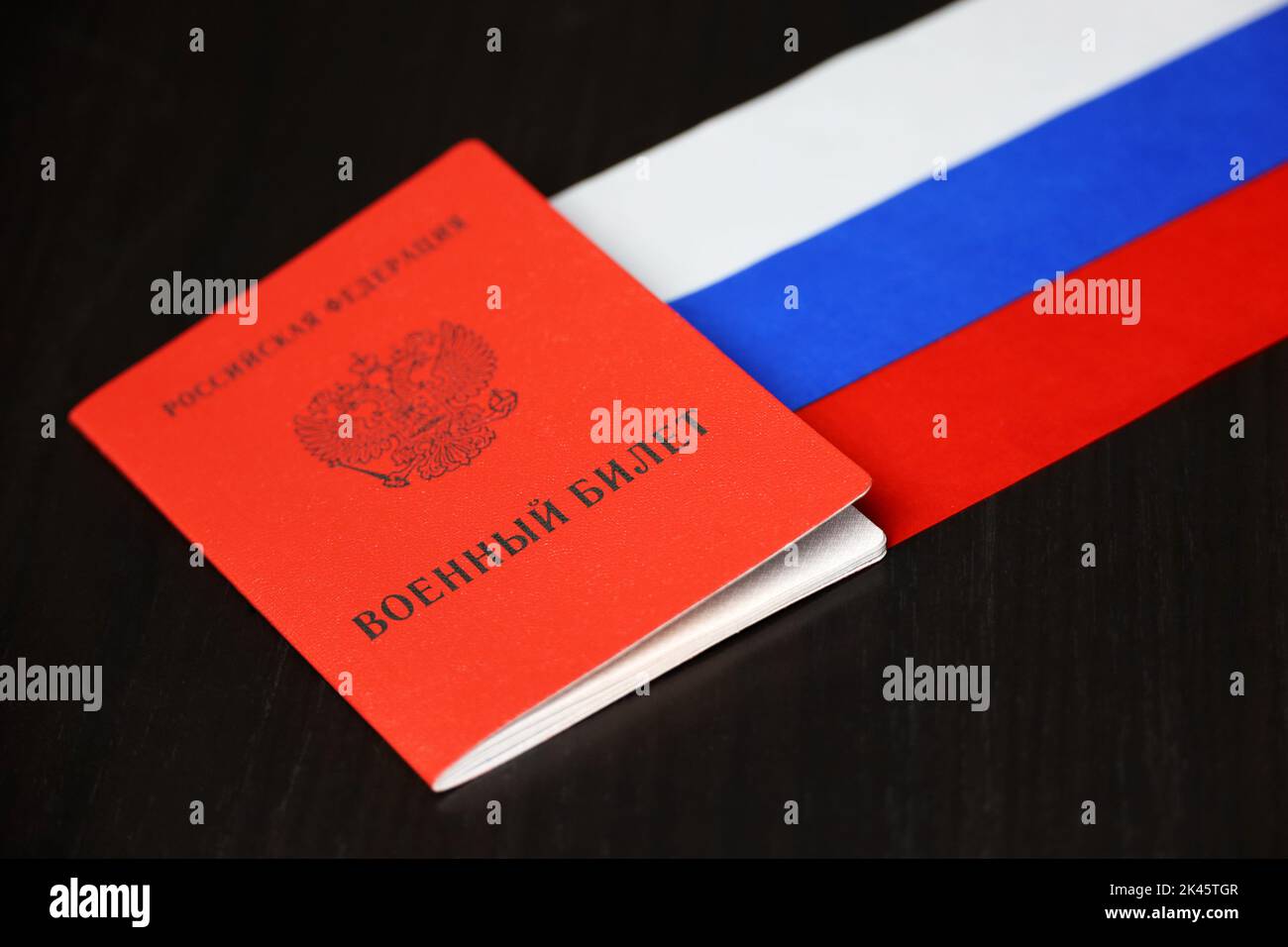 Documento d'identità militare russo e bandiera nazionale su tavolo di legno. Concetto di mobilitazione in Russia Foto Stock