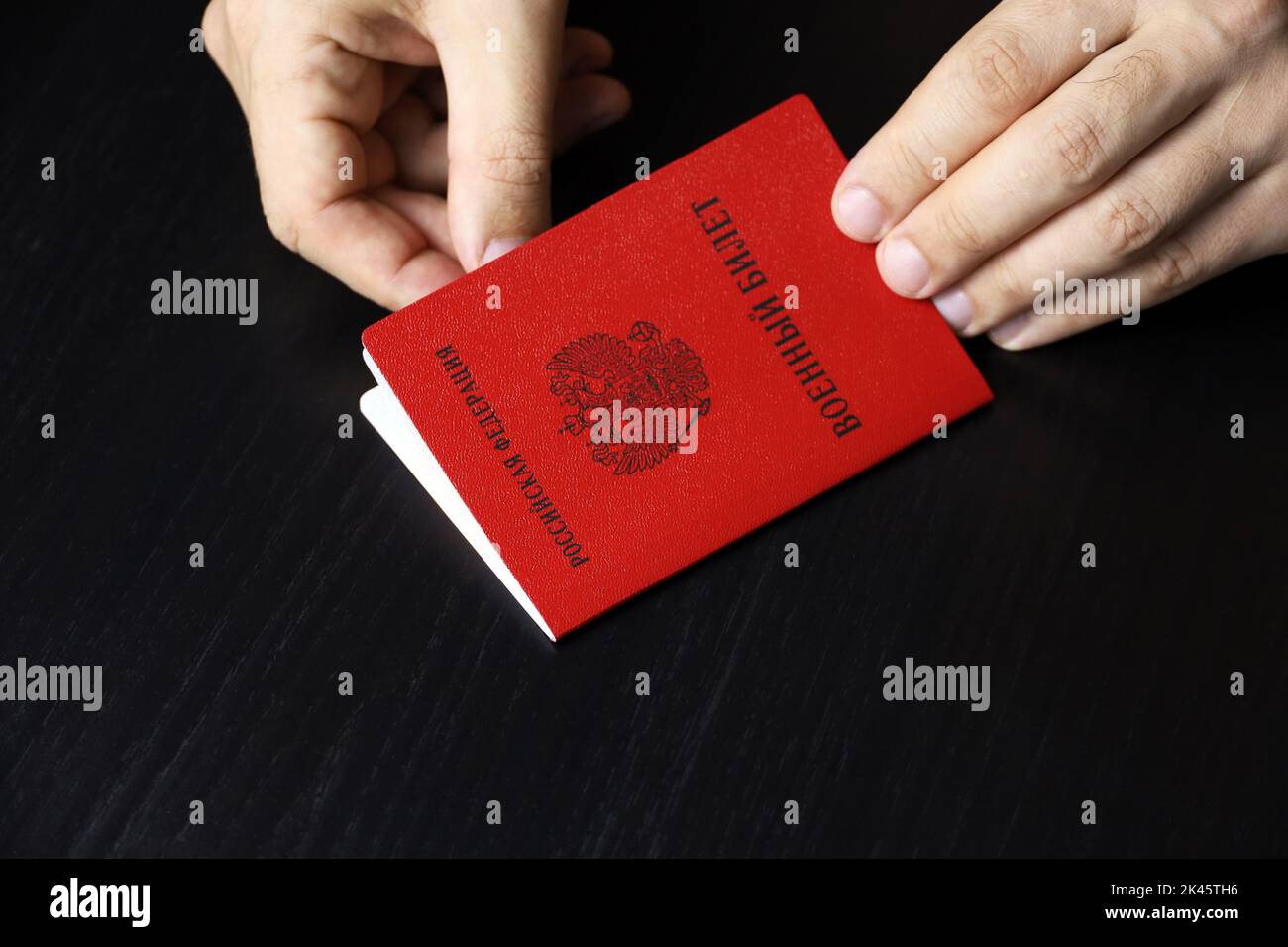 Carta d'identità militare russa in mani maschili su tavolo di legno. Traduzione dell'iscrizione carta d'identità militare, Federazione Russa. Concetto di mobilitazione in Russia Foto Stock
