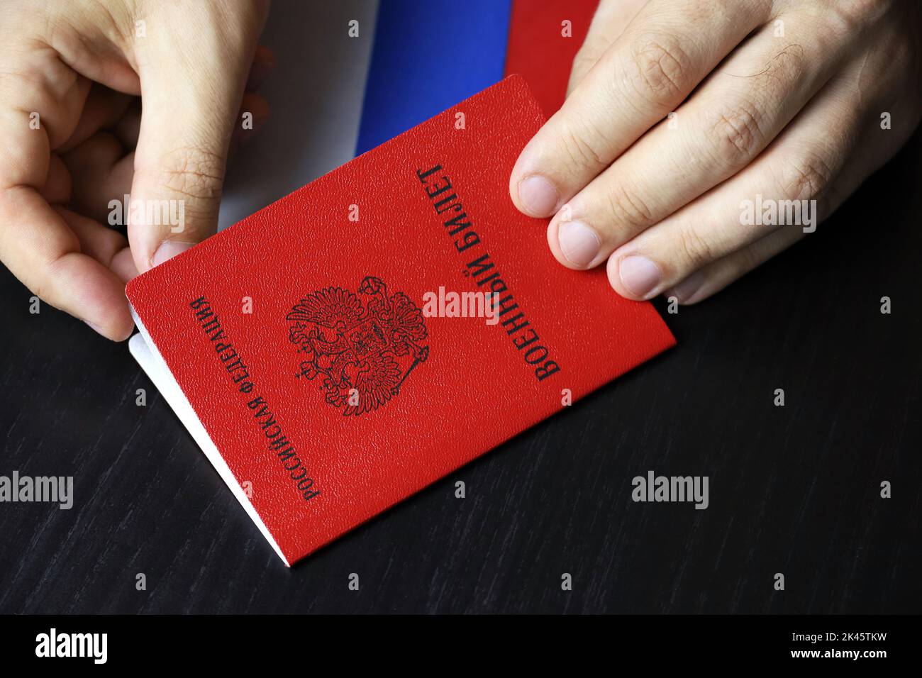 Carta d'identità militare russa in mani maschili su tavolo di legno. Traduzione dell'iscrizione carta d'identità militare, Federazione Russa. Concetto di mobilitazione in Russia Foto Stock