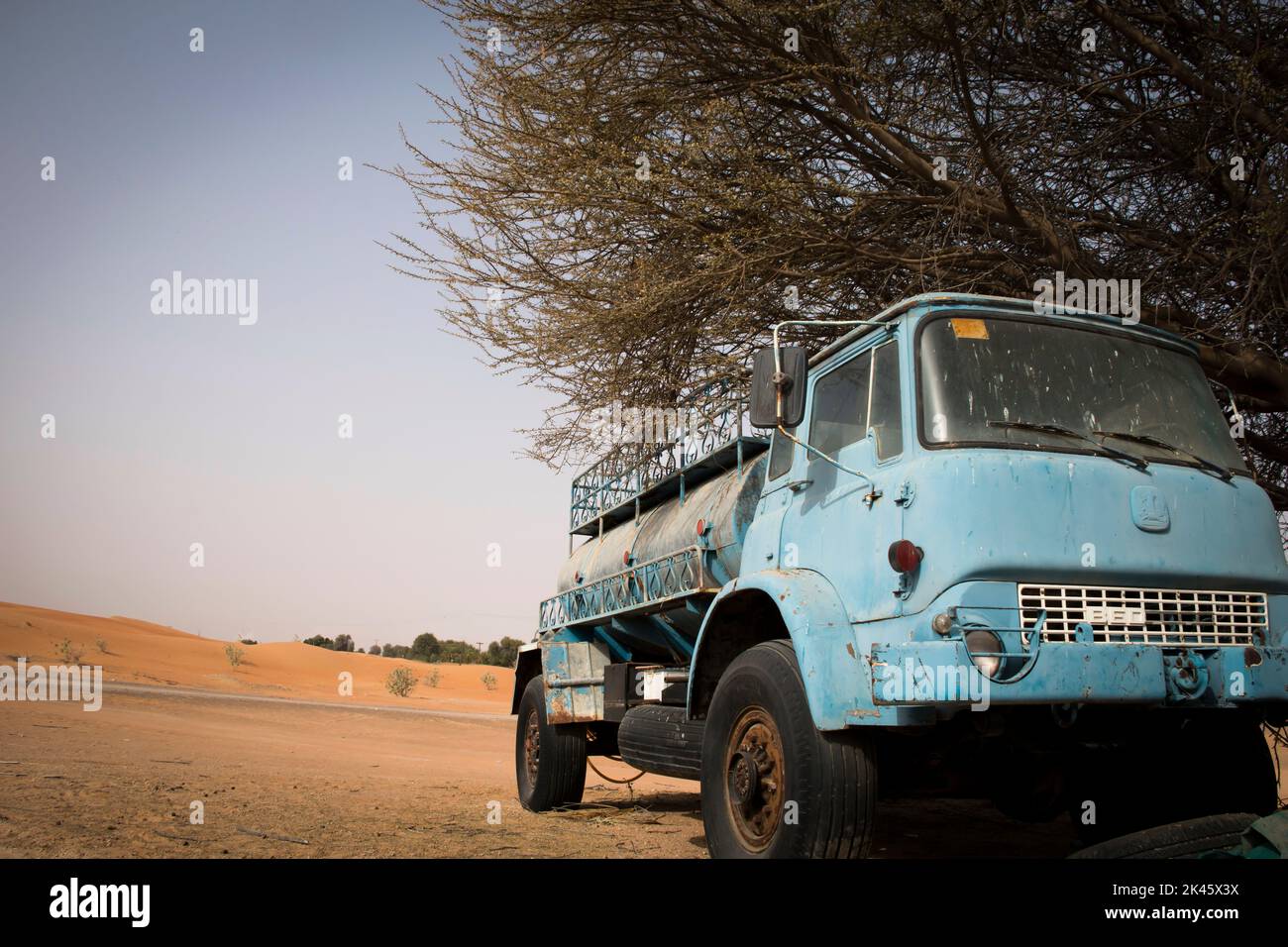 Un vecchio camion di trasporto dell'acqua abbandonato parcheggiato sotto l'albero nel deserto di Dubai Foto Stock