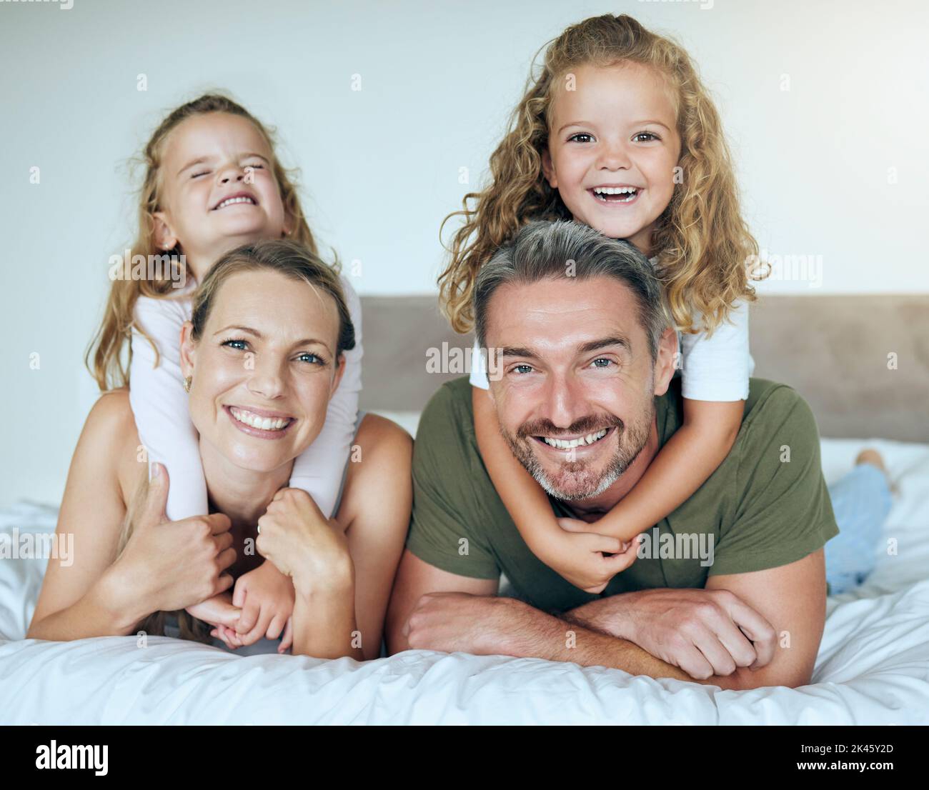 Sorriso di famiglia, ritratto felice e bambini che danno l'amore abbracciare i genitori, felice in vacanza e rilassarsi a letto in casa. Madre e padre con Foto Stock