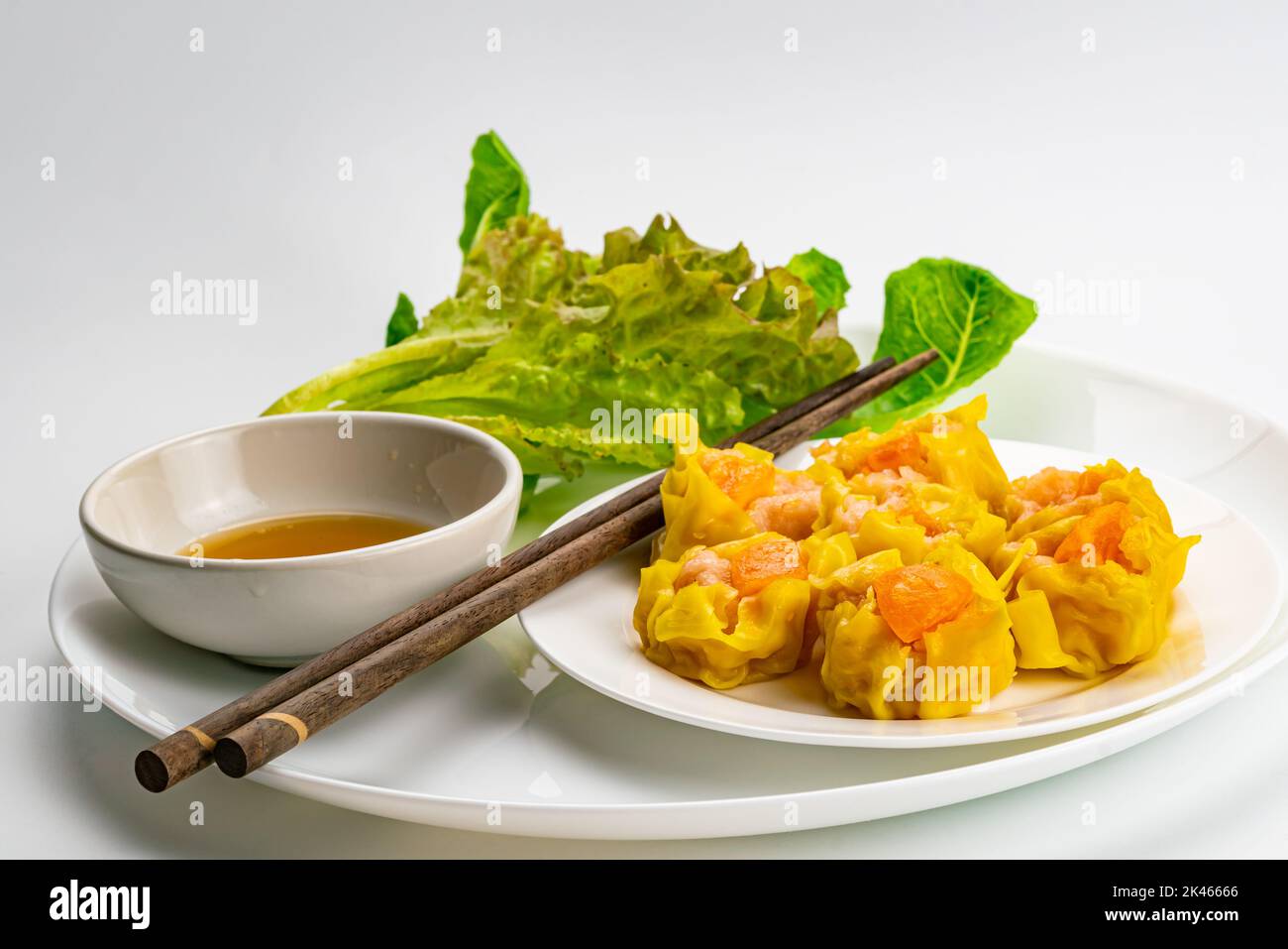 Deliziosi gamberi fatti in casa freschi, maiale tritato e tuorlo d'uovo salato gnocchi al vapore in un piatto di ceramica bianca con salsa in tazza di ceramica bianca, verde fresco Foto Stock