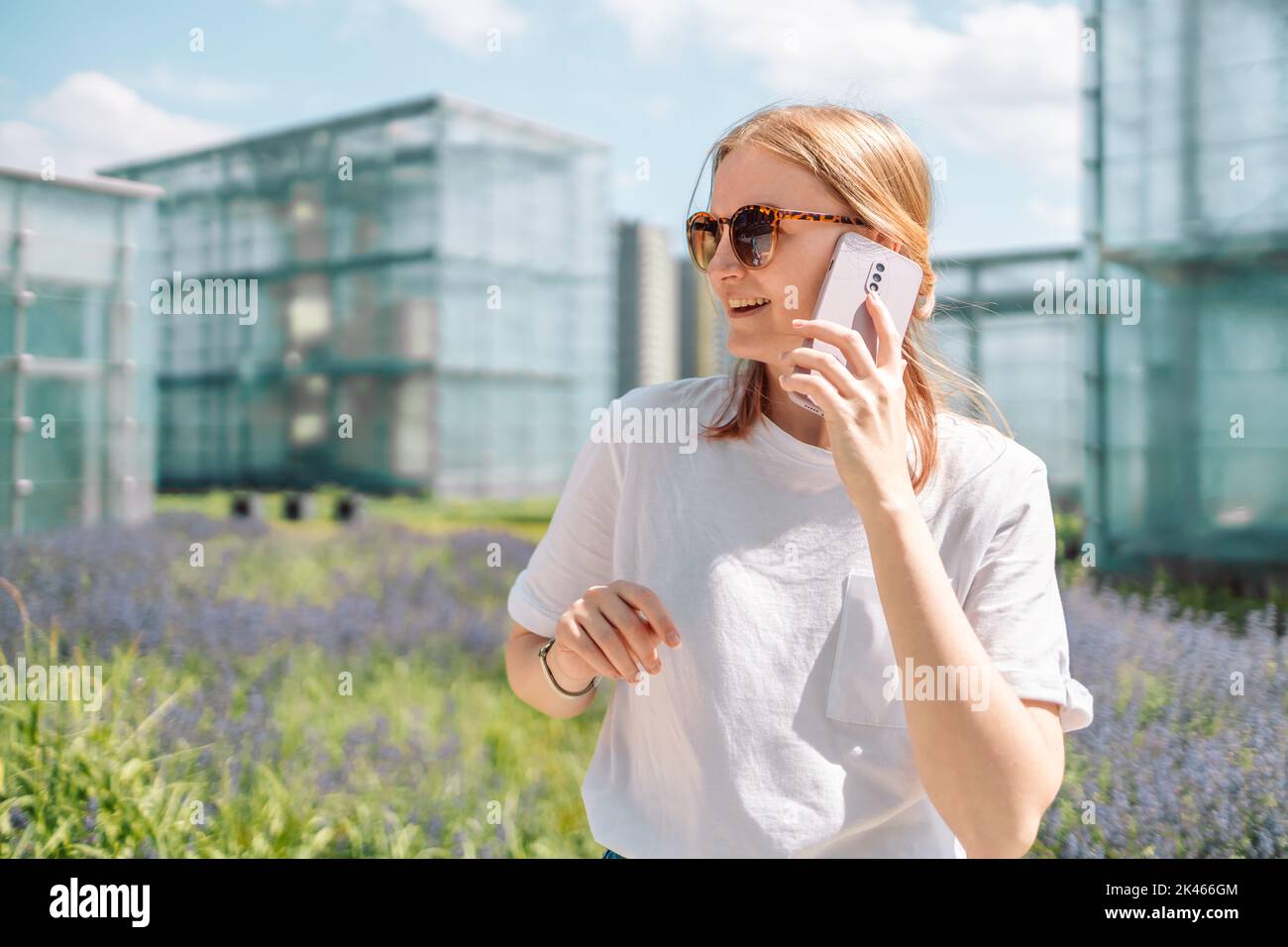 Primo piano di una donna sorridente che parla con qualcuno sul telefono cellulare mentre cammina di fronte al museo Foto Stock