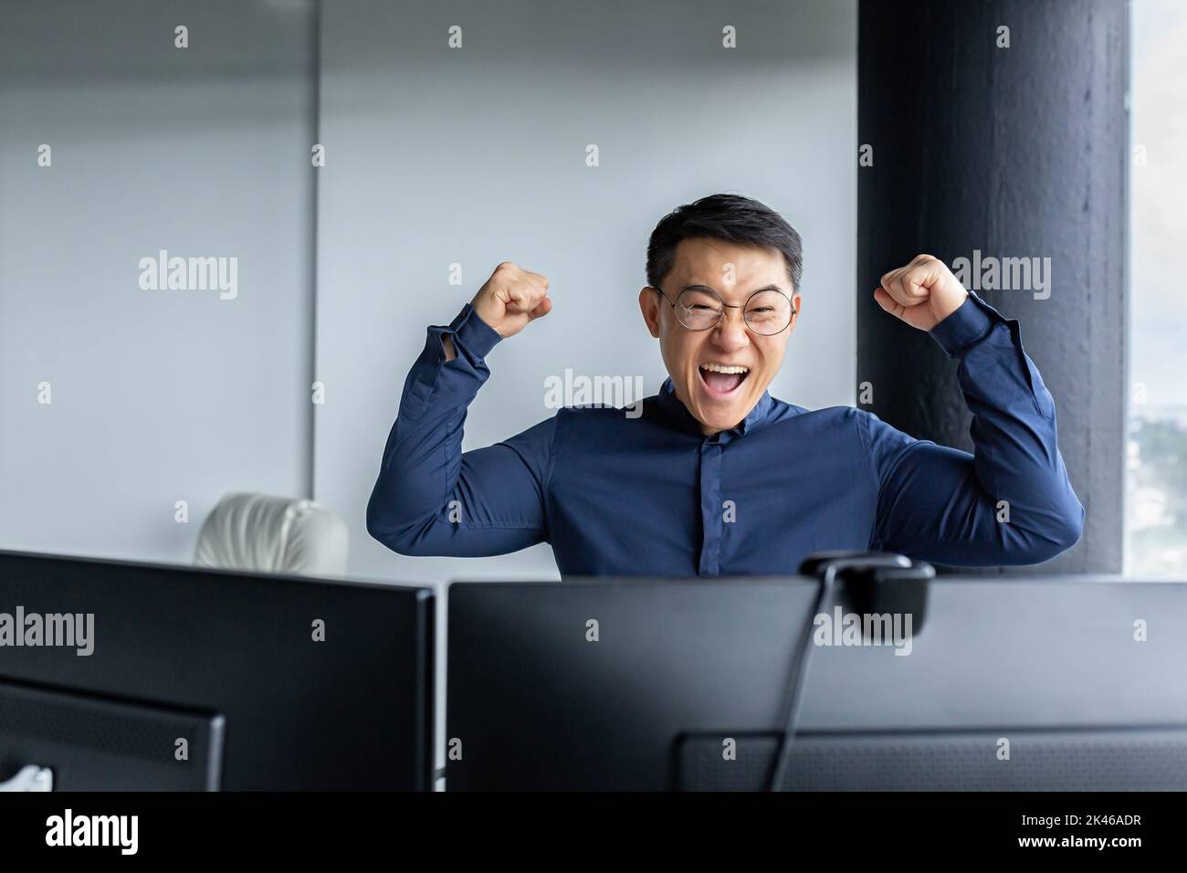 Buon capo asiatico del team di programmatori, guardando lo schermo del computer e felice, celebrando la vittoria, completato il progetto, e presentato il programma completato, imprenditore imprenditore che tiene le mani in su. Foto Stock