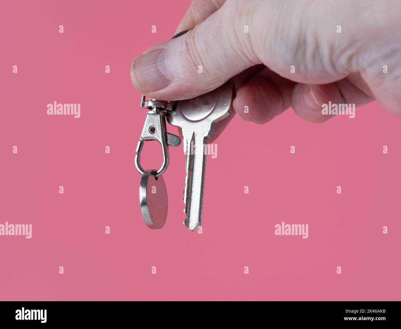 persona che tiene la chiave della porta anteriore ad un nuovo proprty isolato su uno sfondo rosa Foto Stock
