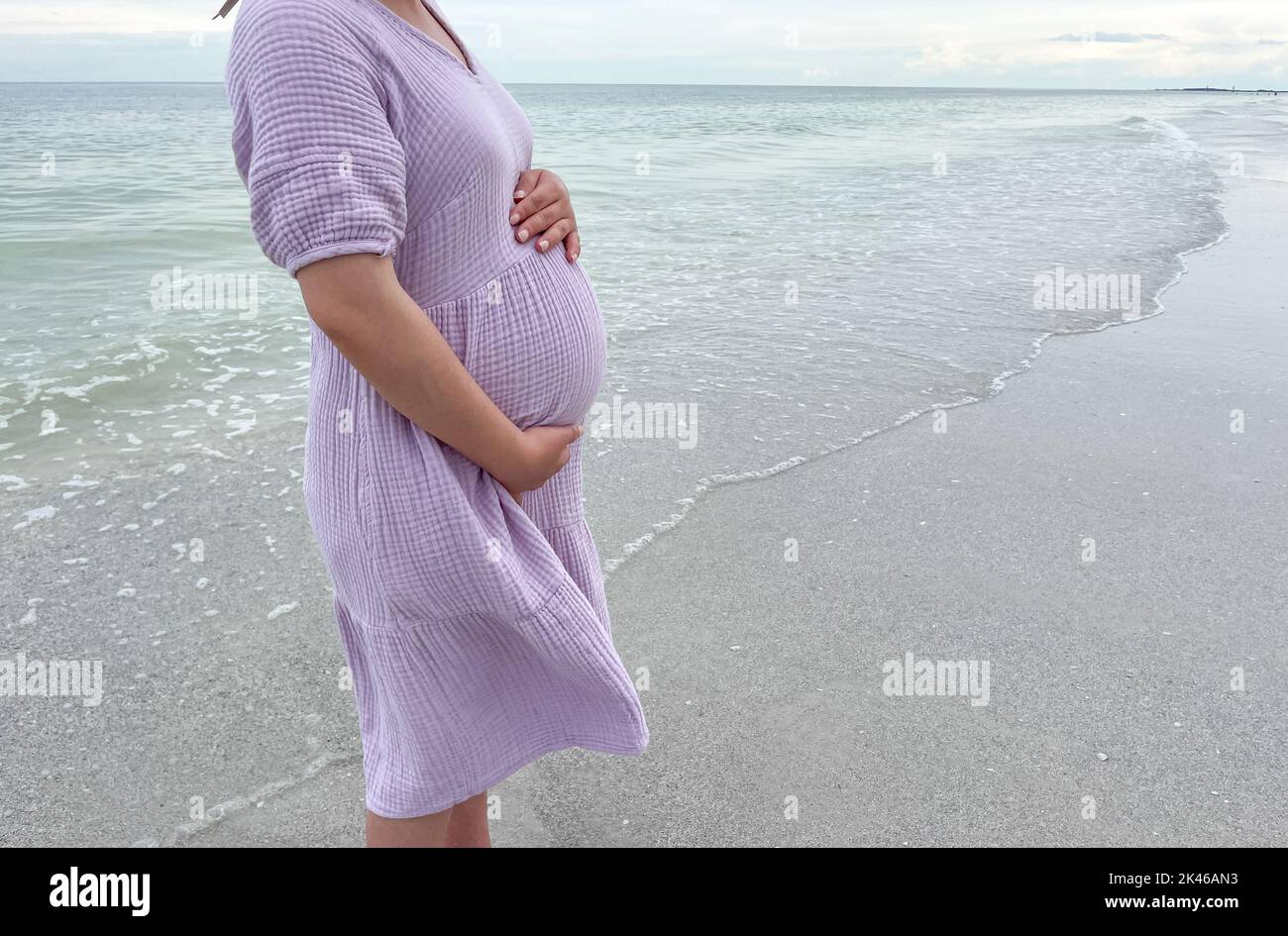 Scatto di una donna incinta in piedi sulla spiaggia con la mano che tiene il suo ventre - gravidanza, aspettativa, concetto di maternità Foto Stock