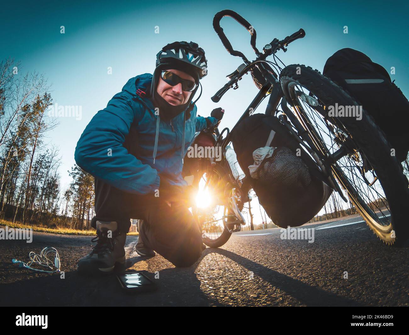 Ciclista sul lato della strada in posa per selfie e tenendo la bicicletta con una mano e con gli accessori a terra. Fotogra grandangolare per sport Foto Stock