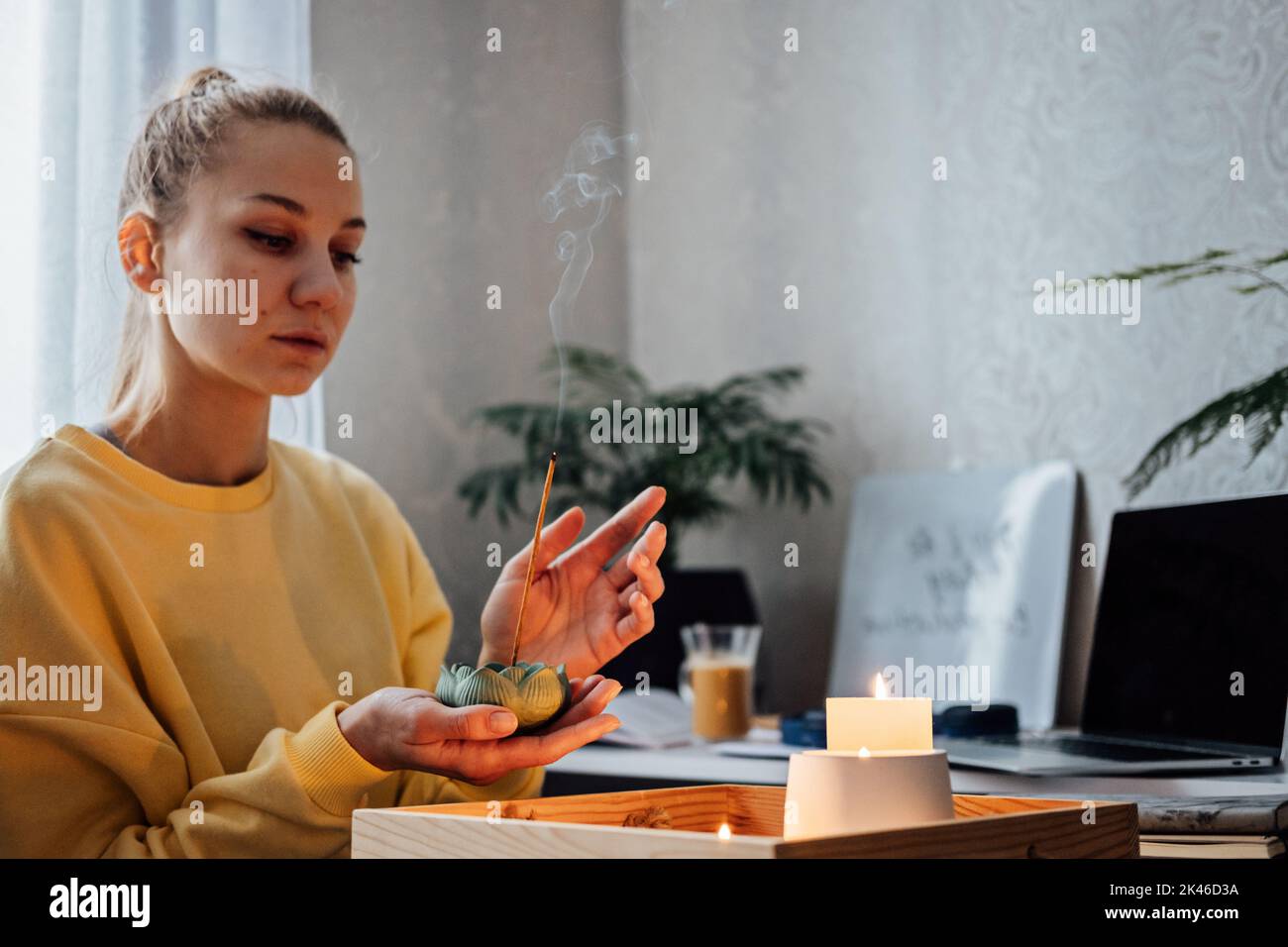 Cura di sé, salute mentale. Giovane donna seduta vicino al tavolo con le candele luci, bastoncini Aroma, godersi la meditazione a casa. Niente stress, abitudini sane Foto Stock