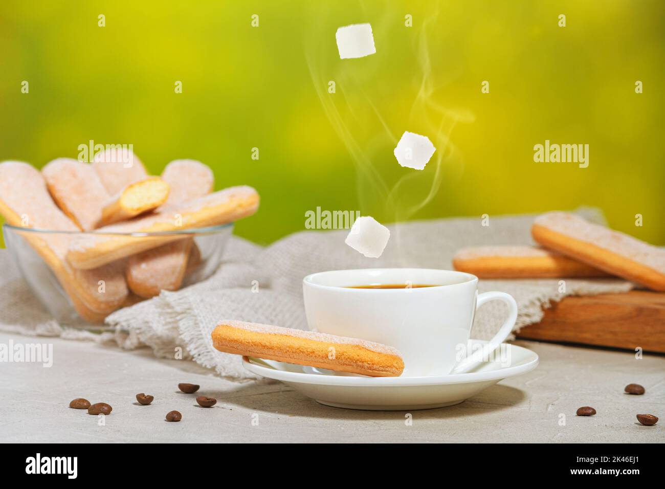 Tazza bianca di caffè aromatico caldo con vapore e cubetti di zucchero cadenti. Biscotti savoiardi tradizionali italiani o biscotti savoiardi su un piatto e in un piatto Foto Stock