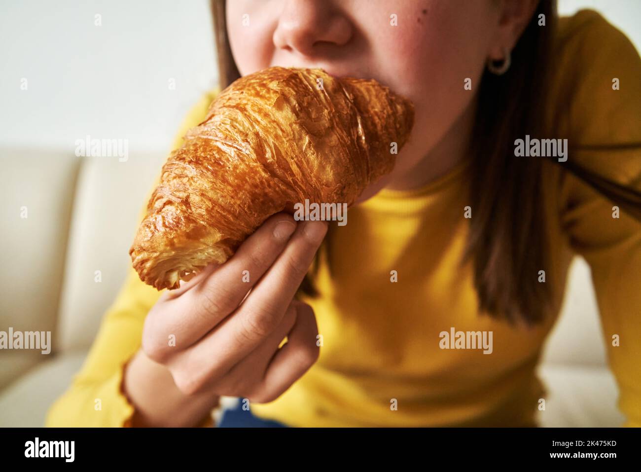 Croissant nelle mani di una ragazza adolescente che prima colazione, primo piano Foto Stock